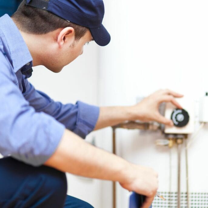 Plumber adjusting the settings on a residential water heater. Keywords: water heater repair, electric and gas water heater maintenance, plumbing services, professional plumber, Dayton OH.