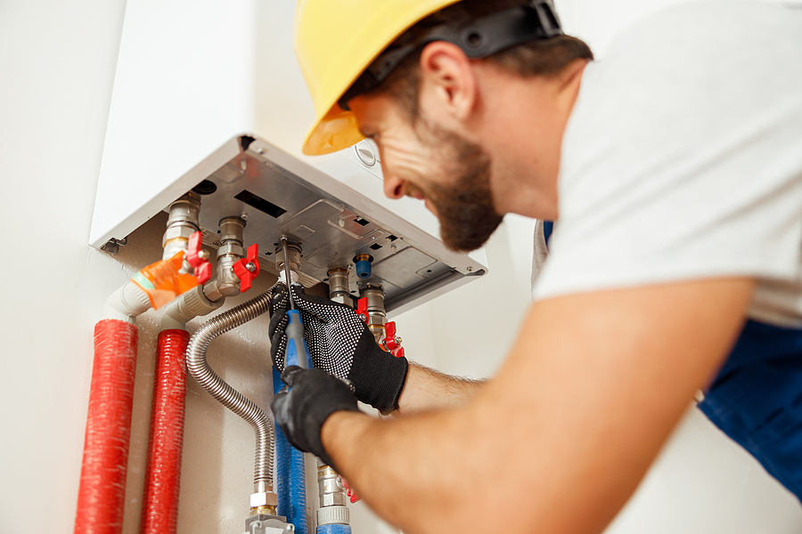 Closeup of a plumber using screwdriver while fixing boiler or water heater.