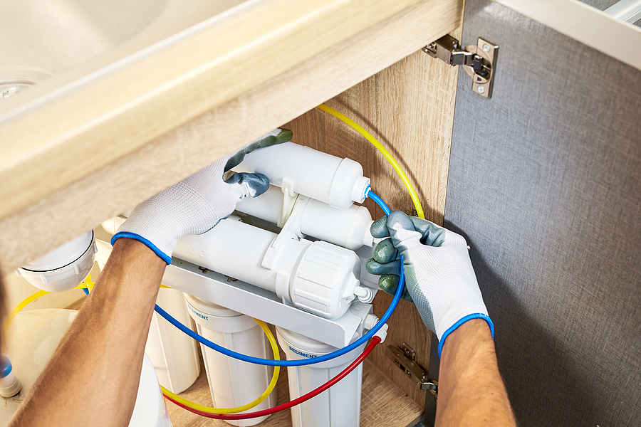 A person replacing water filter cartridges in a reverse osmosis system under a kitchen sink.






